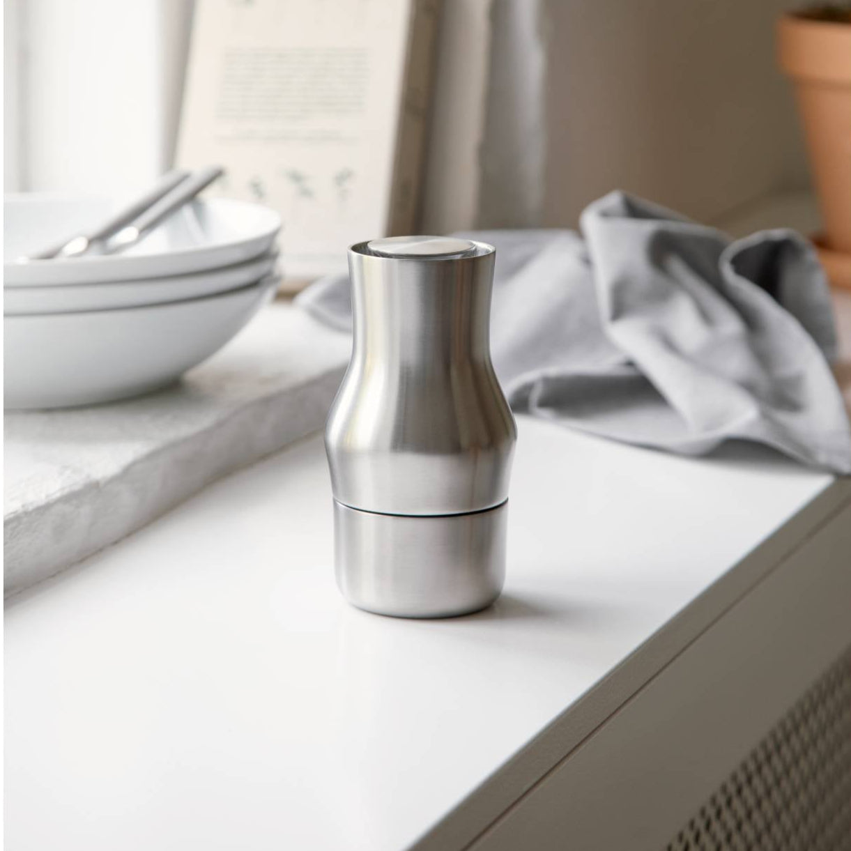 Stainless steel salt grinder on a kitchen counter with bowls and a towel in the background. Gense Dorotea Collection Grinder German Design Award winner