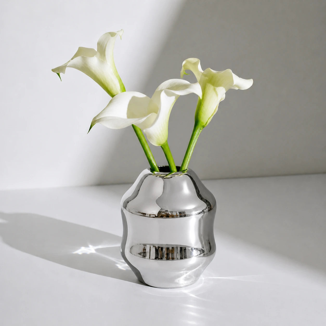 Dorotea Stainless steel vase with white calla lilies on a light surface
