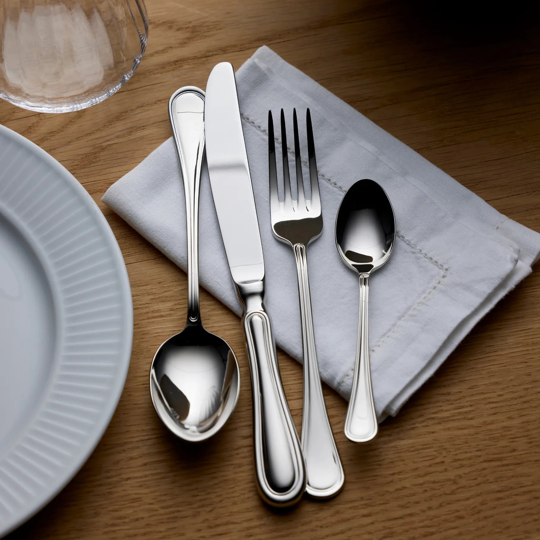 Gense Oxford Silverware set on a wooden table with a white plate and glass. 