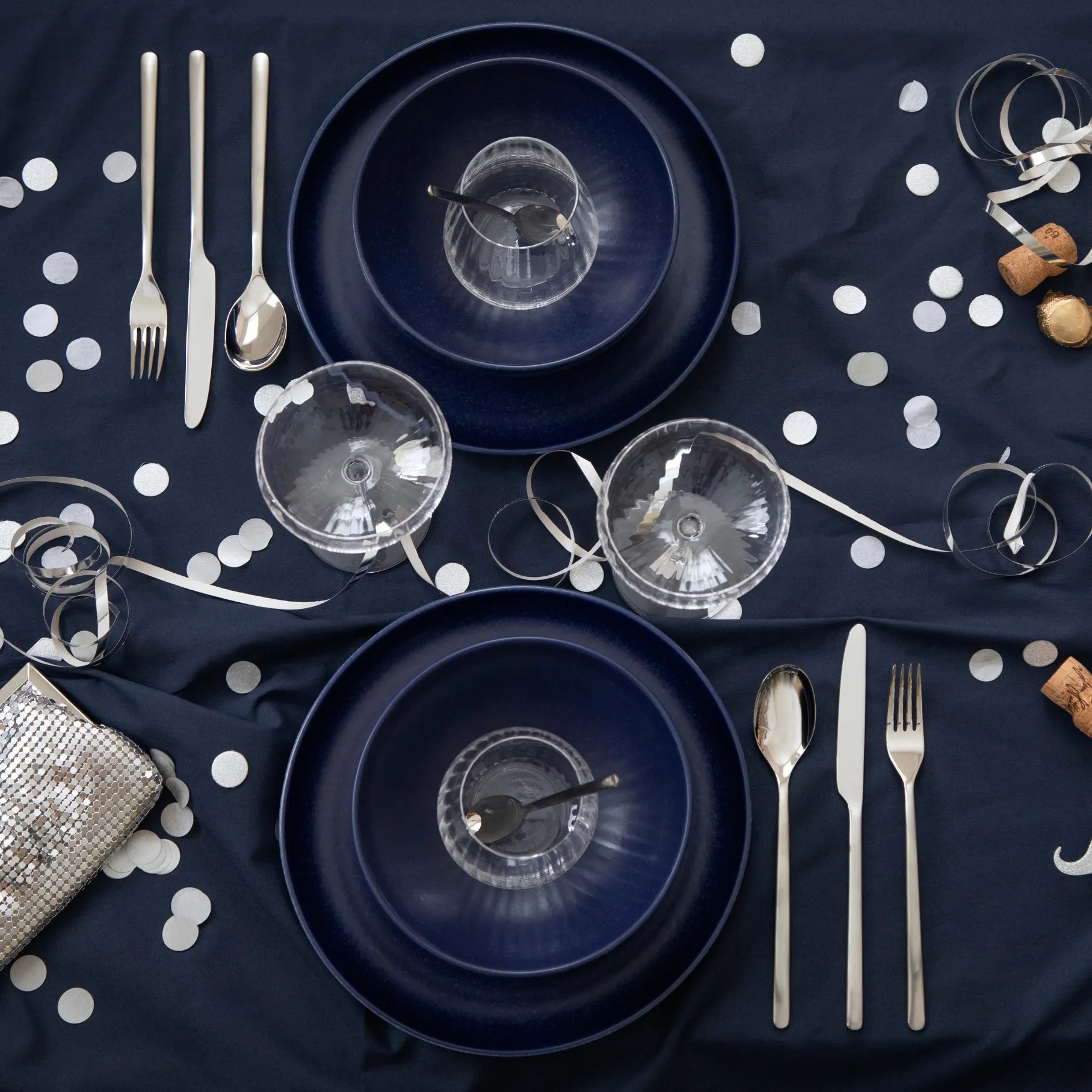 Navy blue plates, Gense Still Collection cutlery, and glasses on a dark surface with white polka dots.